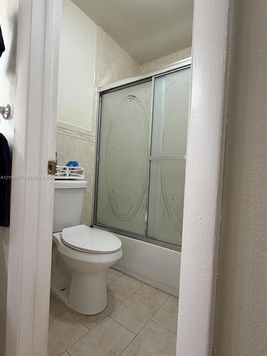 Vanity featuring dark wood cabinetry, integrated stone-finish countertop with an undermount basin, three-light fixture with frosted glass shades, and a decorative tile-framed mirror