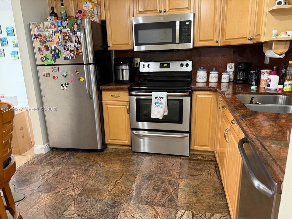 Kitchen featuring natural wood cabinetry, stainless steel appliances, and stone-finish tile flooring