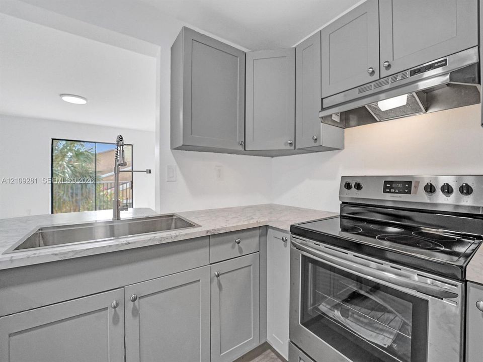 Kitchen featuring grey shaker-style cabinetry, stainless steel range with overhead vent hood, stone-finish countertops, and an undermount sink with a gooseneck faucet
