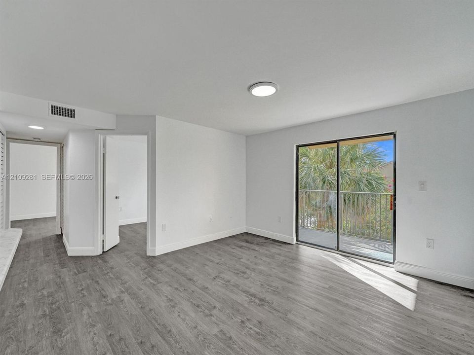 Interior space featuring wood-finish flooring, neutral walls, flush-mount ceiling lighting, and a sliding glass door providing external access to a railed balcony