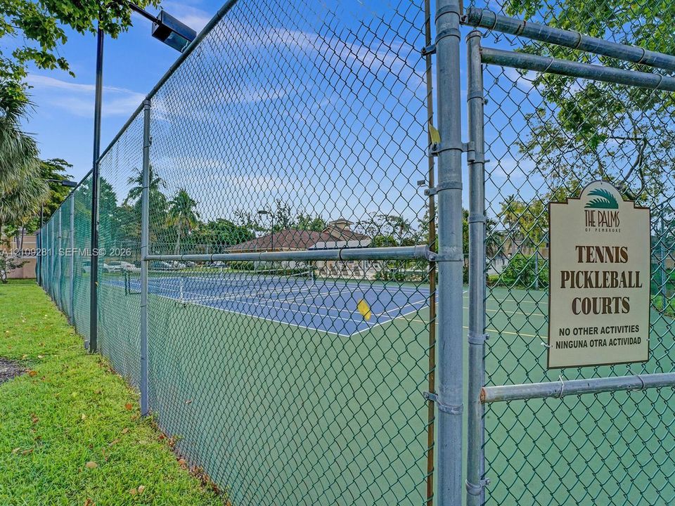 Multi-use sports court featuring designated tennis and pickleball play areas, chain-link fencing, and overhead court lighting