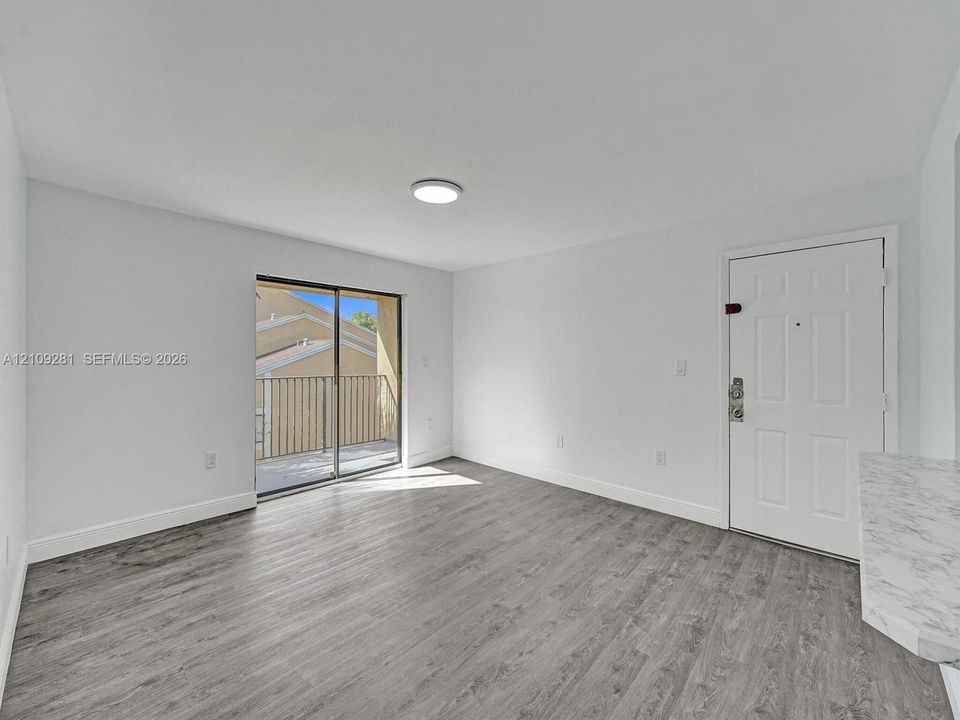 Interior space featuring wood-finish flooring, sliding glass door with access to a private balcony, white paneled entry door, and flush-mount ceiling lighting