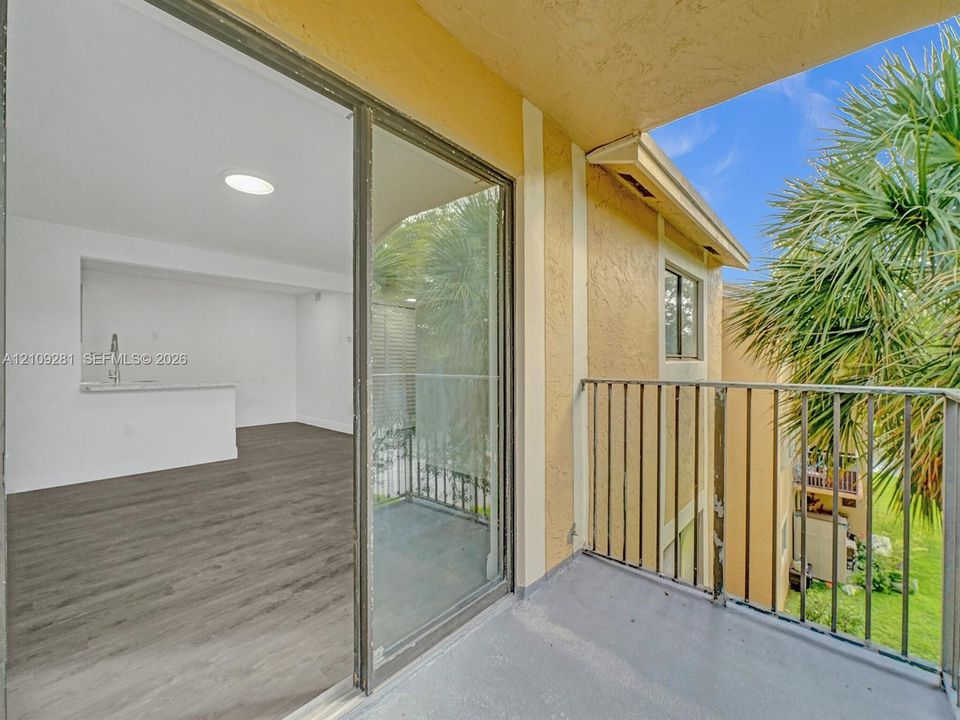 Covered balcony featuring metal railings, sliding glass door entry, wood-finish flooring, and a pass-through opening to a kitchen area