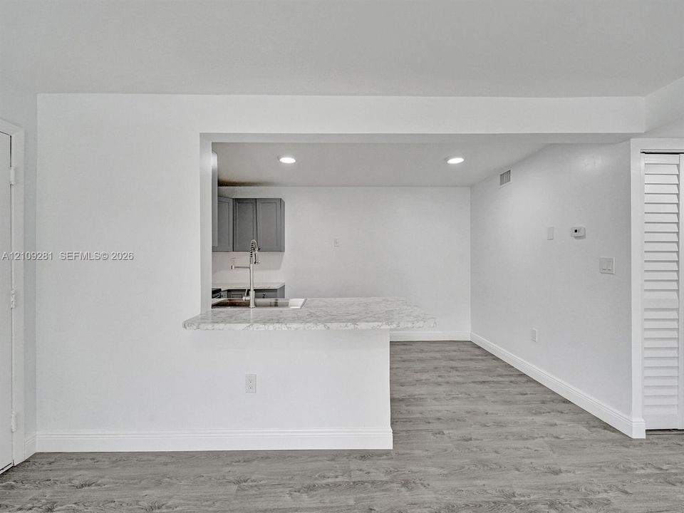 Pass-through opening with a stone-finish countertop, recessed lighting, wood-finish flooring, and louvered closet doors