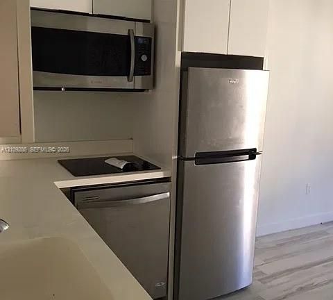 Kitchen featuring white cabinetry, solid-surface countertops, and a suite of stainless steel appliances including a refrigerator, dishwasher, and microwave