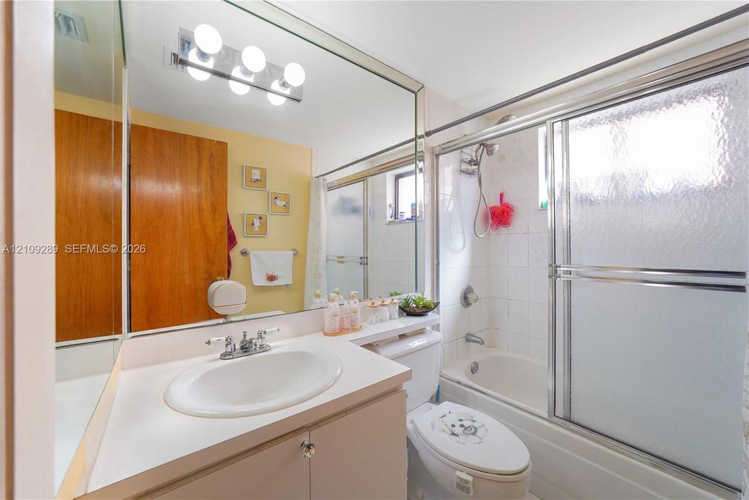 Full-width wall mirror, vanity with integrated sink, four-light vanity fixture, and a tub-shower combination enclosed by sliding glass doors