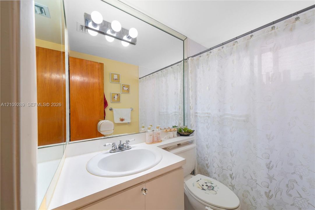 Bathroom featuring a white integrated sink with a dual-handle faucet, vanity cabinet with neutral finish, full-width wall mirror, and four-bulb overhead vanity lighting