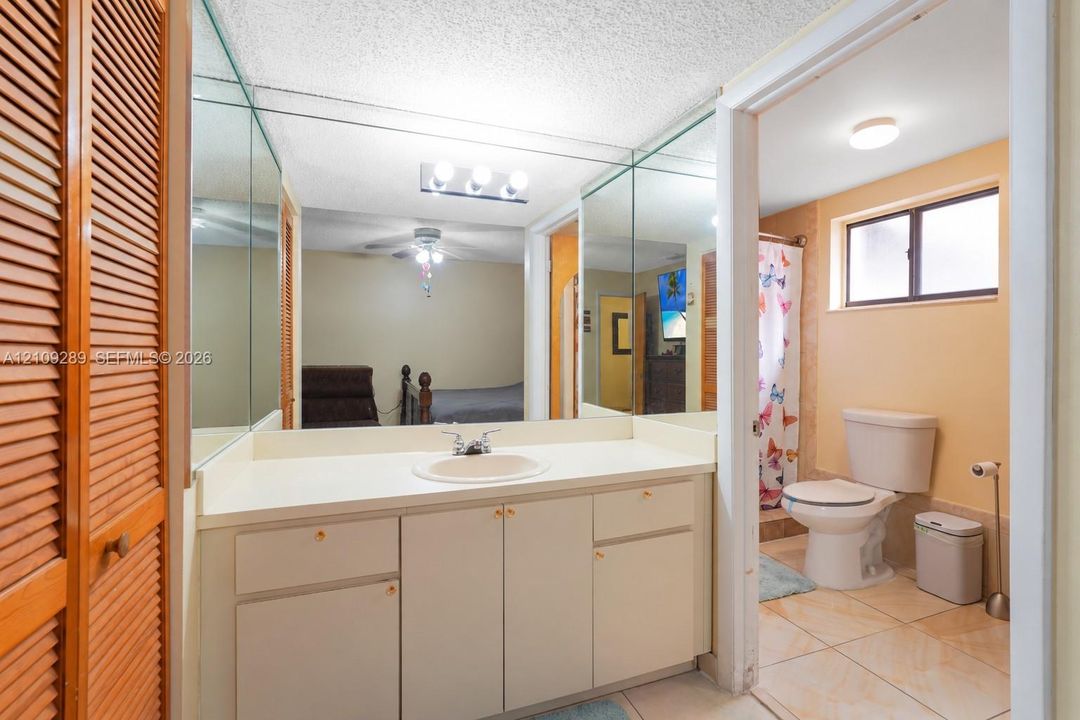 Bathroom featuring a vanity with an integrated sink, full-width wall mirror, wood-slat closet doors, and ceramic tile flooring