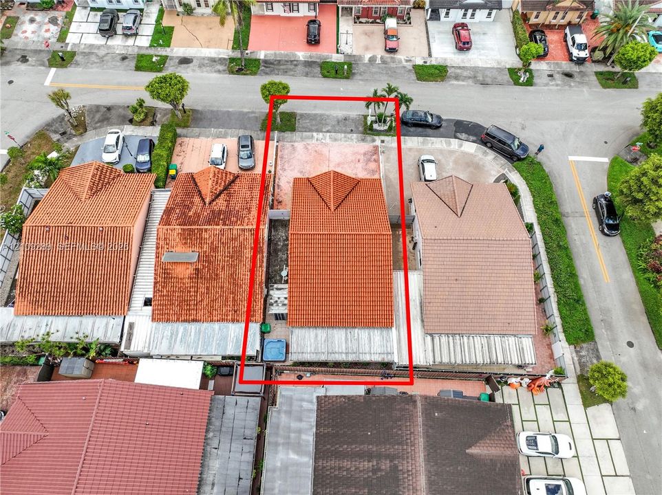 Aerial perspective of a property featuring a terracotta-tiled roof, an integrated concrete driveway, and a fenced rear perimeter