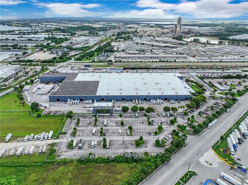 Industrial facility featuring a large-scale warehouse structure, paved expansive parking area, multiple loading bays, and direct access to regional transit infrastructure