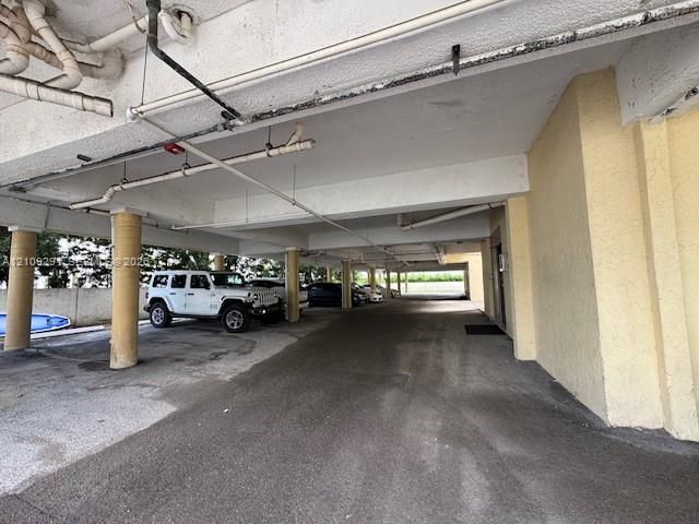 Covered parking area featuring concrete support pillars, paved ground surface, and overhead structural ceiling