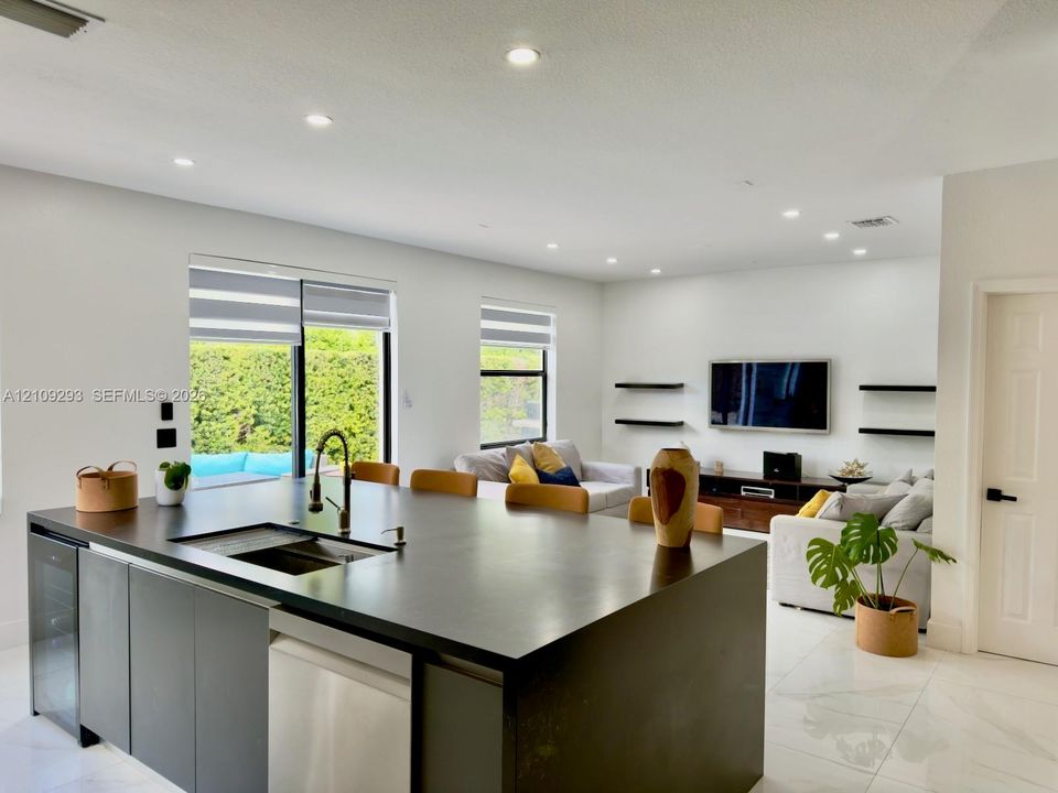 Kitchen island featuring a stone countertop, under-mount sink with a pull-down faucet, integrated wine refrigerator, and light-colored tile flooring