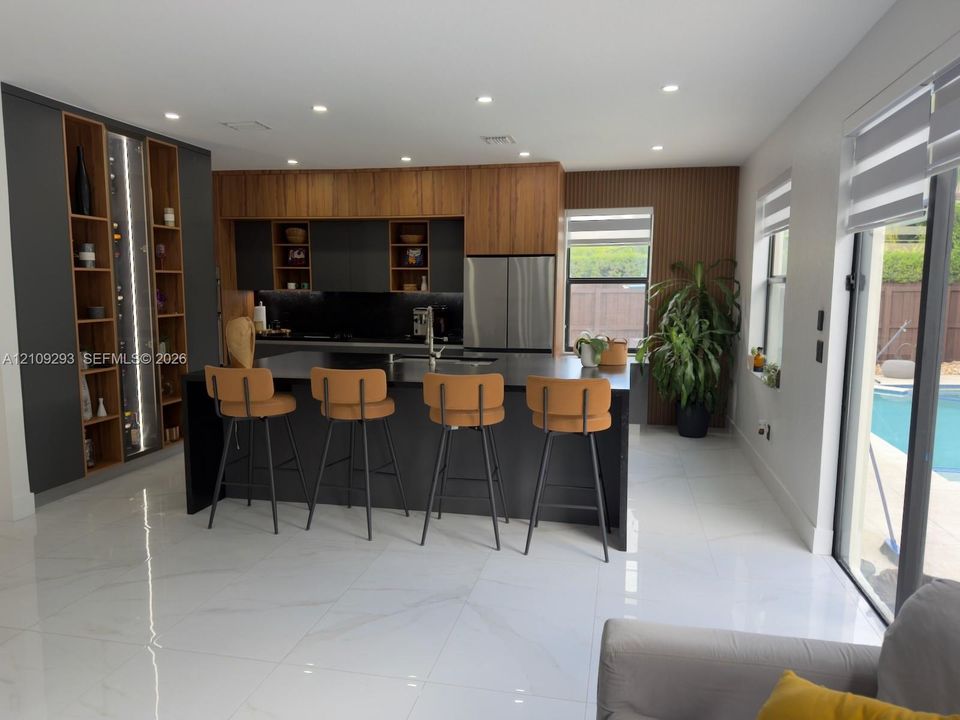 Kitchen featuring custom cabinetry with wood-finish and matte-black accents, central island with dark stone countertop, integrated floor-to-ceiling shelving, recessed lighting, and large-format tile flooring