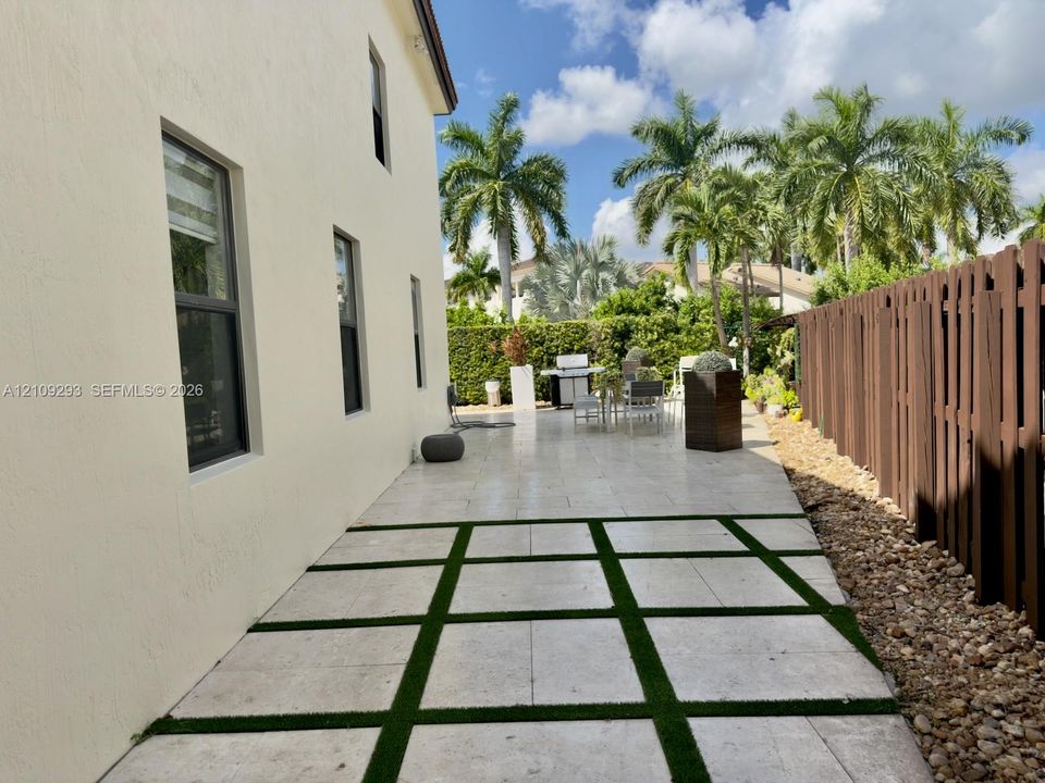 Outdoor patio featuring large-format light-toned pavers with integrated turf grid, perimeter privacy fencing, and exterior stucco siding