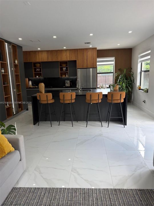 Kitchen featuring a center island, matte dark cabinetry with wood-finish upper detailing, recessed lighting, and large-format porcelain tile flooring