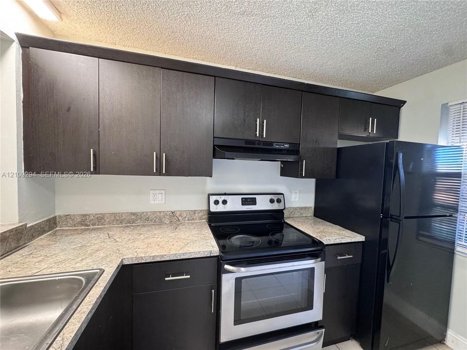Kitchen featuring dark cabinetry, stone-finish countertops, stainless steel electric range, and integrated black refrigerator