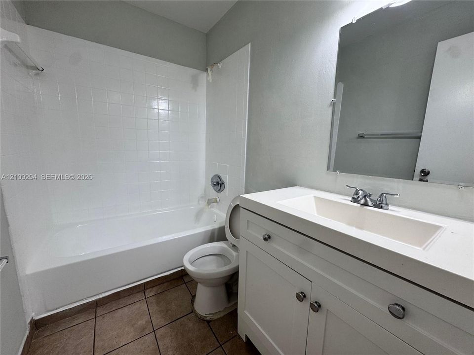 Bathroom featuring a white vanity cabinet with an integrated rectangular sink, wall-mounted mirror, white tub-shower combination with tile surround, and tile flooring