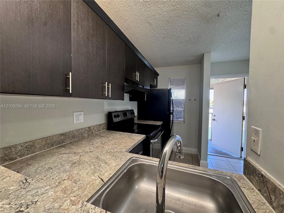 Kitchen featuring dark-toned cabinetry with brushed metal hardware, stone-finish countertops, stainless steel undermount sink with a gooseneck faucet, and black appliance suite