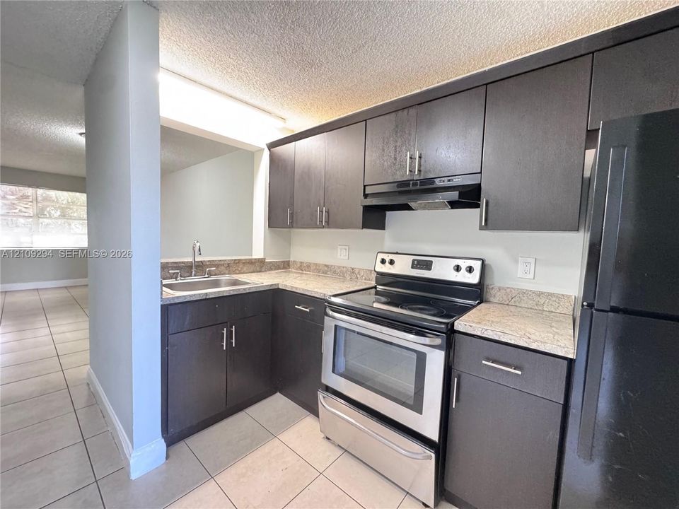 Kitchen featuring dark cabinetry, stone-finish countertops, tile flooring, stainless steel electric range, and a pass-through opening