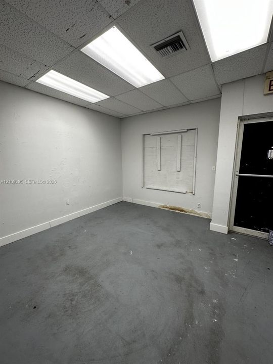 Interior space featuring a suspended drop ceiling, recessed panel lighting, gray painted concrete flooring, and a glass-paneled entry door
