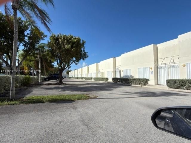 Commercial exterior featuring concrete tilt-wall construction, metal roll-up doors, paved surface parking, and mature perimeter landscaping