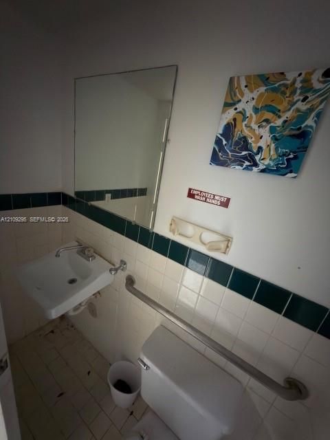 Wall-mounted sink with chrome faucet, large rectangular mirror, and horizontal metal grab bar, featuring cream-colored wall tiles with a dark green accent border