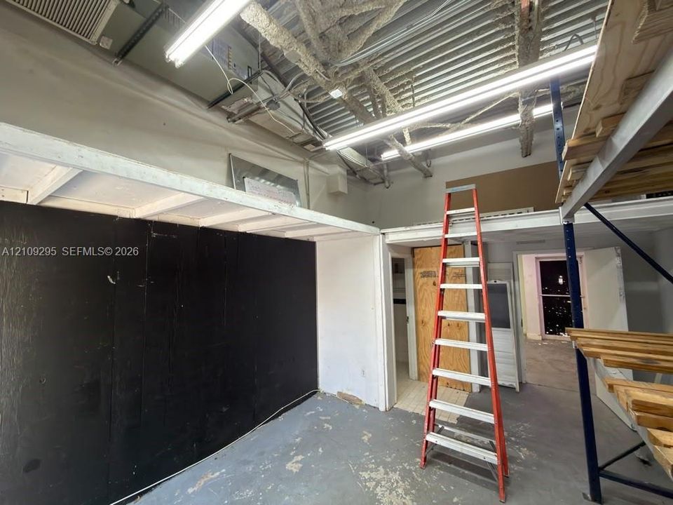 Industrial-style interior featuring exposed corrugated metal ceiling, high-output linear lighting, built-in wooden shelving structure, and painted wood paneling
