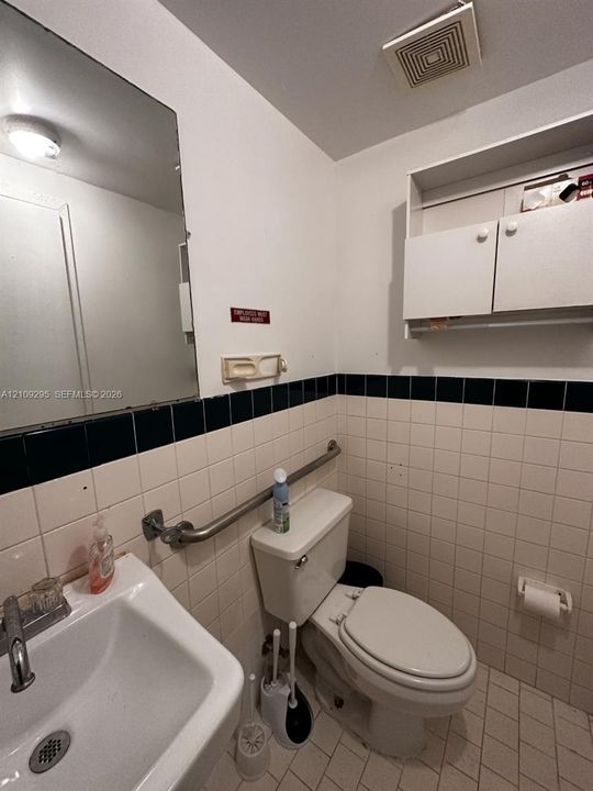 Wall-mounted storage cabinetry, ceramic tiled walls with dark accent trim, wall-mounted metal grab bar, and wall-mounted vanity mirror