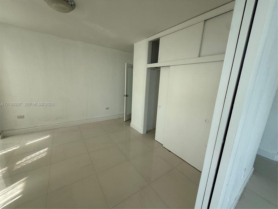 Room featuring large-format tile flooring, ceiling-mounted lighting, and built-in floor-to-ceiling closet cabinetry with sliding doors