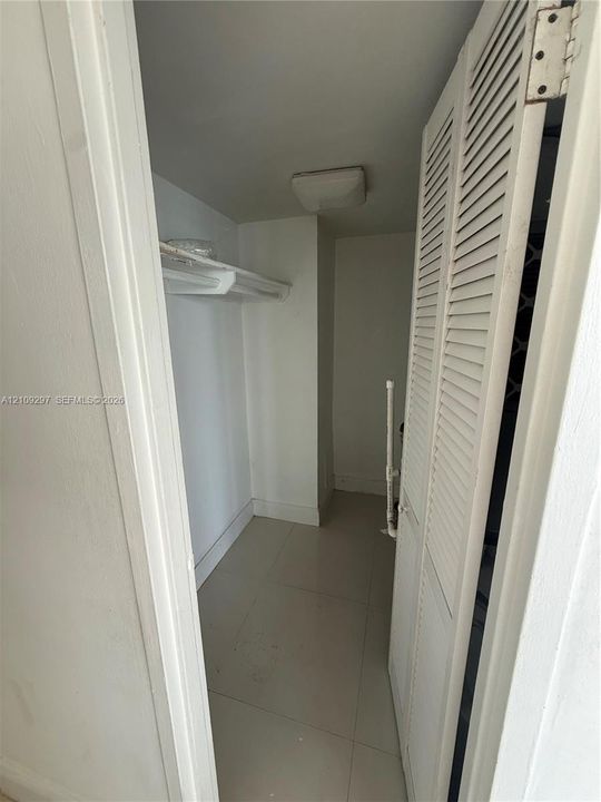 Storage closet featuring louvered bi-fold doors, white shelving, tile flooring, and a flush-mount light fixture