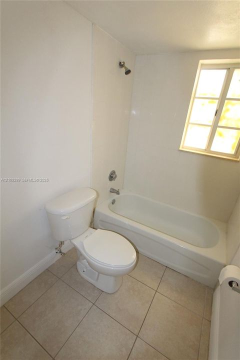 Bathroom featuring ceramic tile flooring, white porcelain tub and shower combination, polished metal fixtures, and a dual-pane window