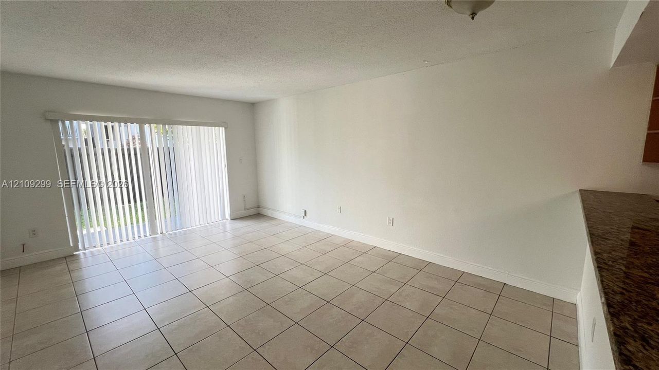 Interior space featuring light-toned ceramic tile flooring, sliding glass door with vertical blinds, and stone-finish countertop