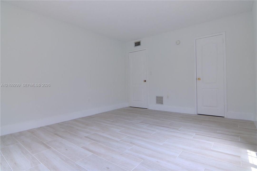 Neutral interior featuring wood-finish flooring, white walls, and two raised-panel doors with metallic hardware