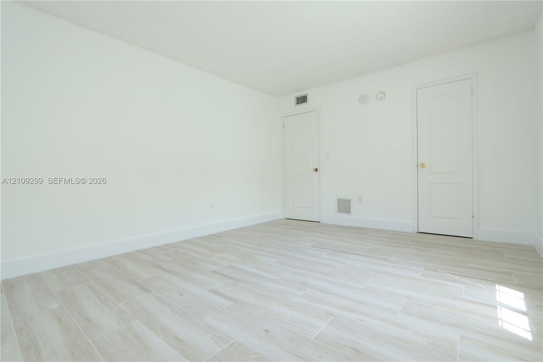 Interior space featuring neutral wall paint, wood-finish tile flooring, and two interior doors with brass hardware