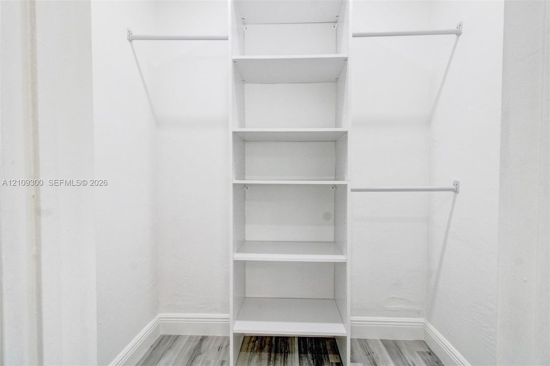 Walk-in closet featuring white built-in shelving, dual-level garment rods, and wood-finish flooring