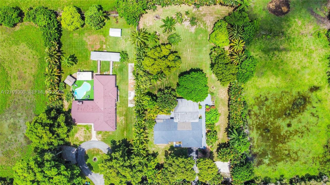 Aerial perspective of a sprawling property featuring two distinct residential structures, a swimming pool, mature perimeter landscaping, and expansive acreage