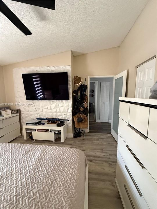 Vaulted ceiling with a central fan, textured three-dimensional wall paneling, and wood-finish flooring
