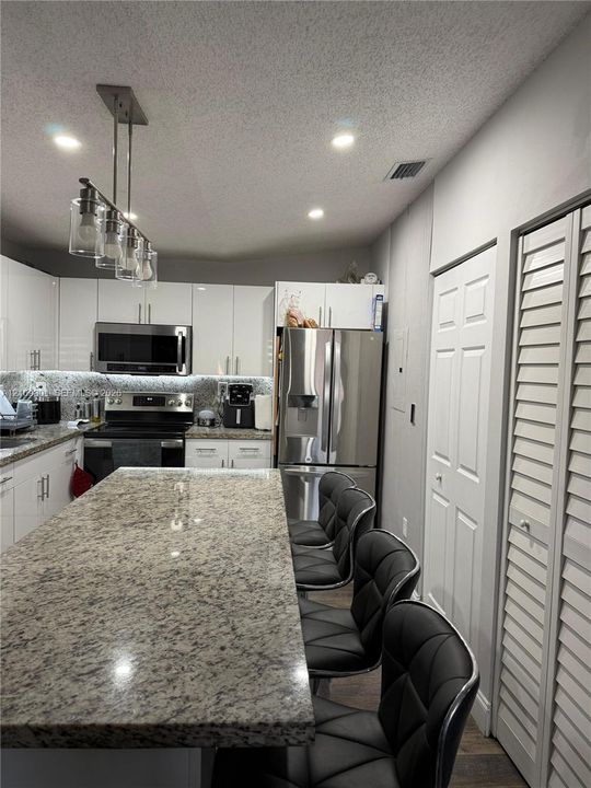 Kitchen featuring a large central island with stone countertop, gloss-finish cabinetry, stainless steel appliances, and a multi-light pendant fixture