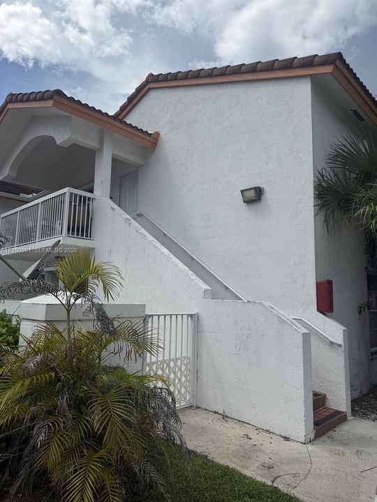 Stucco exterior featuring a tiled roof, upper-level balcony with metal railing, and concrete staircase with integrated handrail