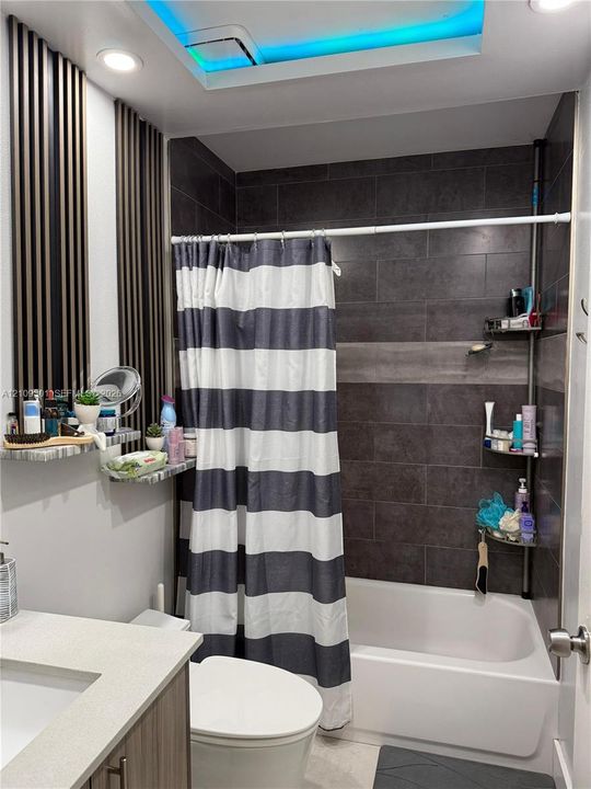 Bathroom featuring large-format dark charcoal tile shower surround, integrated LED ceiling lighting, vertical slat wall accents, and vanity with solid-surface countertop