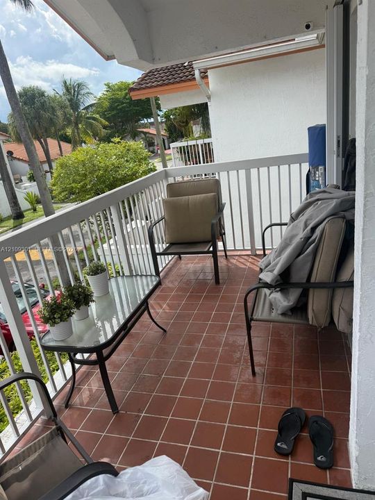 Covered balcony featuring terracotta-style tile flooring and white vertical railings