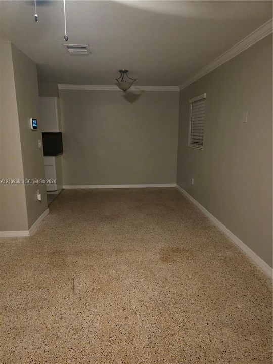 Interior space featuring neutral-toned walls, crown molding, a central semi-flush mount light fixture, and terrazzo flooring