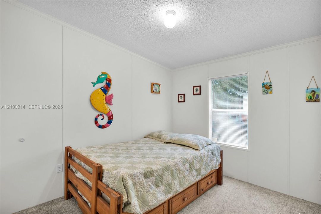 Neutral-toned wall paneling, wall-to-wall carpeting, single-pane window with horizontal blinds, and a central ceiling-mounted light fixture