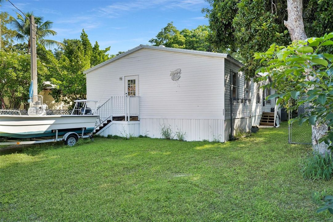 Exterior featuring light-colored horizontal siding, a multi-pane glass entry door, metal staircase railing, and a private yard with mature trees