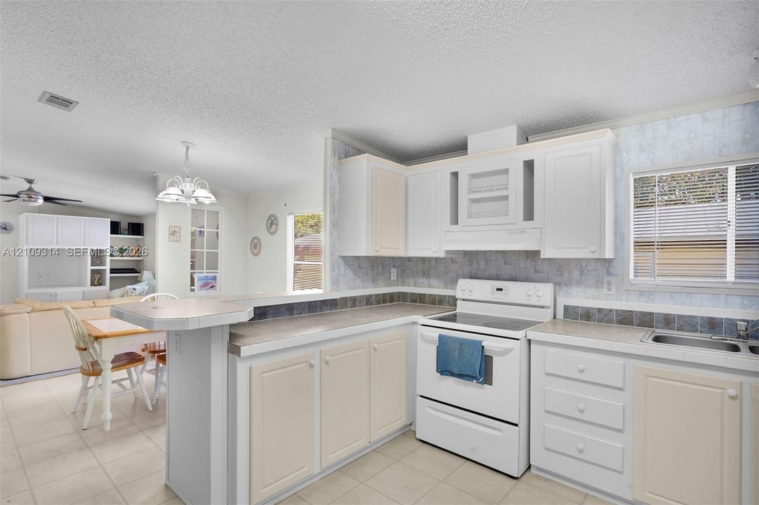 Kitchen featuring a breakfast bar, white shaker-style cabinetry, a range with an integrated vent hood, tile backsplash, and ceramic tile flooring