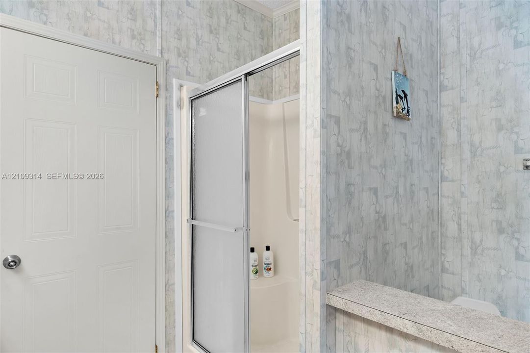 Shower enclosure with a metal-framed sliding glass door and a molded surround, six-panel interior door with a circular knob, and a stone-finish countertop