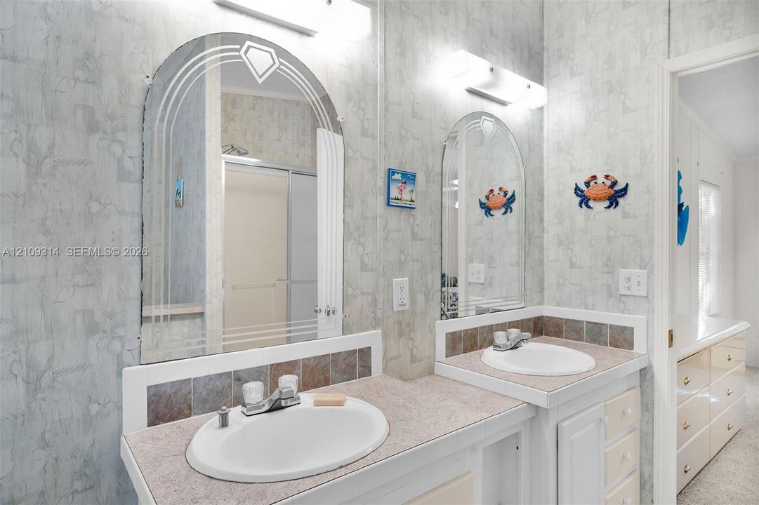 Dual-sink vanity with speckled countertop, decorative tile backsplash, arched mirrors with etched detailing, and integrated wall-mounted lighting