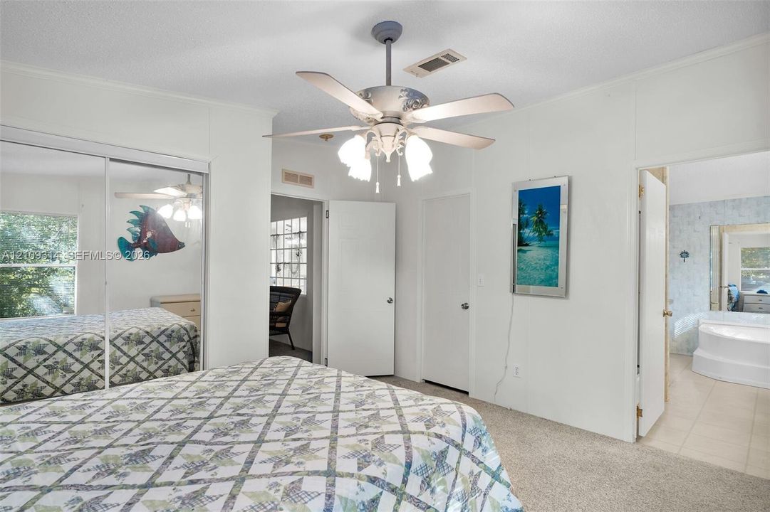 Room featuring wall-to-wall carpeting, mirrored sliding closet doors, a multi-light ceiling fan, and access to a bathroom with a soaking tub