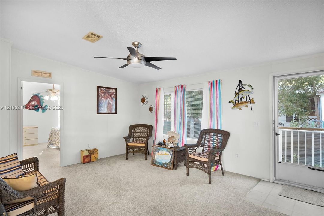 Neutral-toned interior featuring wall-to-wall carpeting, a multi-blade ceiling fan with integrated lighting, and a glass-panel exterior door