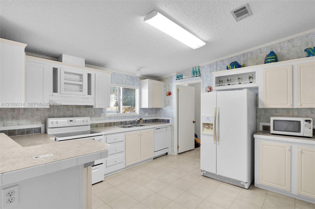 Kitchen featuring white cabinetry, solid-surface countertops, tile flooring, integrated appliances, and a built-in display shelf above the refrigerator